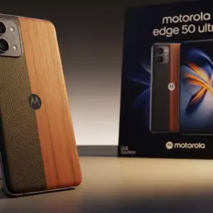 Motorola Edge 50 Ultra placed on a studio table with soft lighting, showing wood and vegan-leather finishes, U.S. launch poster in background